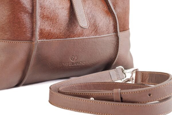 cartera-clarisse-gamuza-pelo-vaca-cuero-chocolate-detalle-logo-correa-rose-blanche.jpg Detalle logo Rose Blanche estampado y correa larga removible, Cartera Clarisse gamuza pelo vaca y cuero chocolate, artesanal Patagonia