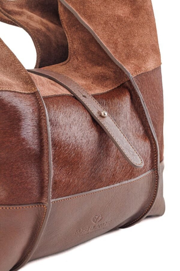 cartera-clarisse-gamuza-pelo-vaca-cuero-chocolate-detalle-lateral-texturas-rose-blanche.jpg Detalle lateral Cartera Clarisse Rose Blanche, combinación de pelo de vaca y cuero vacuno chocolate con tira central, artesanal Patagonia